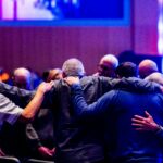 A congregation of men embracing and praying together in a church setting.