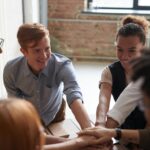 A diverse group of young professionals joining hands in a cheerful and supportive team-building activity.