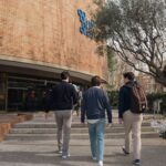 Three students approach a university building entrance in Barcelona, Spain on a sunny day.