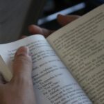 A person reading a book, focusing on the text and hands, in a cozy indoor setting.